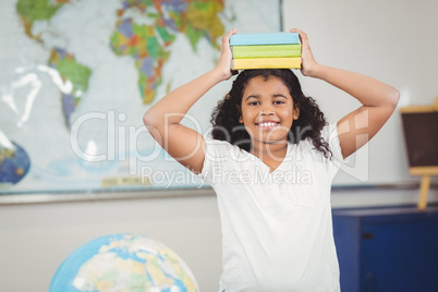 Smiling pupil balancing books on head in a classroom