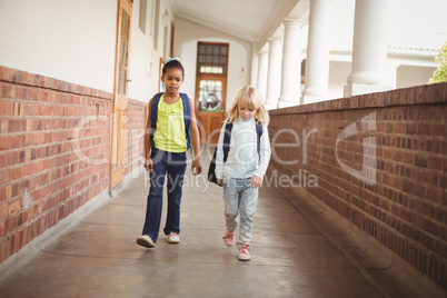 Cute pupils walking with schoolbags at corridor