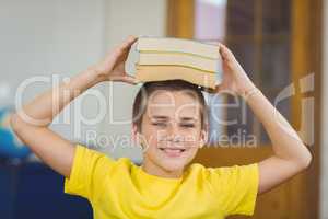 Smiling pupil balancing books on head in a classroom
