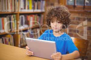 Cute pupil using tablet in the library