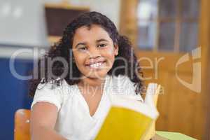 Smiling pupil reading book in a classroom