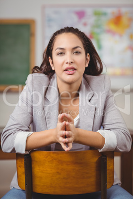 Pretty teacher sitting on chair in a classroom