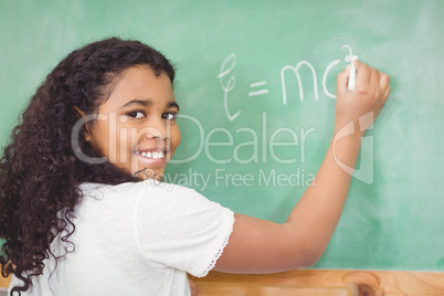 Smiling pupil writing on chalkboard in a classroom