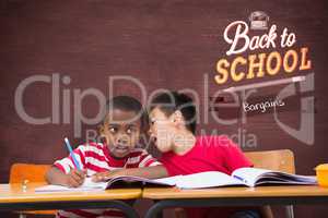 Composite image of cute pupils writing at desk in classroom