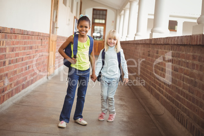 Smiling pupils holding hands at corridor