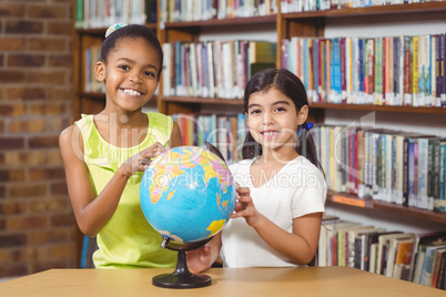 Smiling pupils studying globe in the library