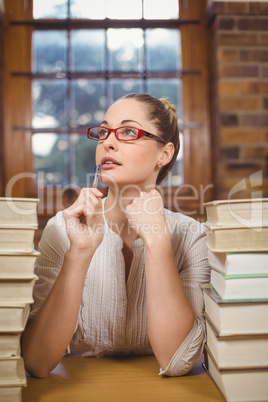 Thoughtful blonde teacher sitting between books in the library