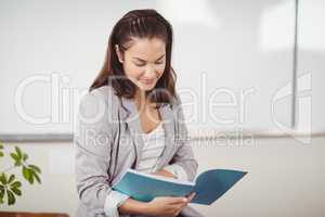 Pretty teacher reading book and sitting on desk