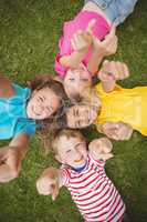 Smiling classmates lying in grass and pointing to camera