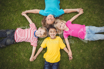 Smiling classmates lying in grass and holding hands