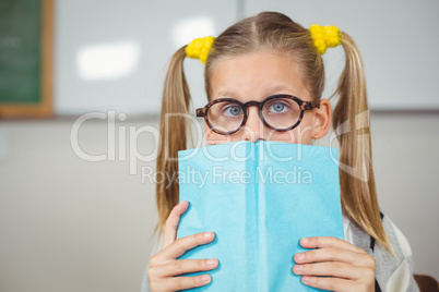 Cute pupil covering face with a book in a classroom