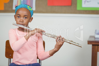 Cute pupil playing flute in a classroom