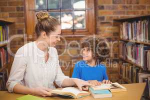 Blonde teacher and pupil reading books in the library