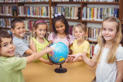 Pupils smiling at camera in library pointing to globe