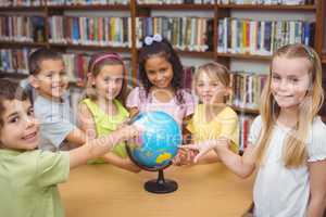 Pupils smiling at camera in library pointing to globe