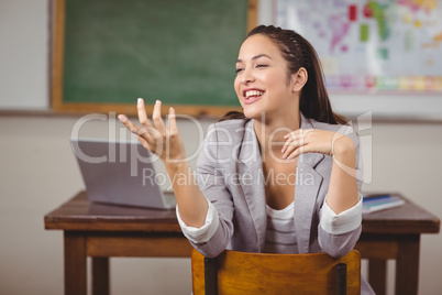 Pretty teacher sitting on chair and talking in a classroom