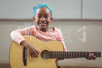 Smiling pupil playing guitar in a classroom