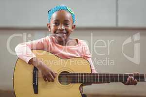 Smiling pupil playing guitar in a classroom