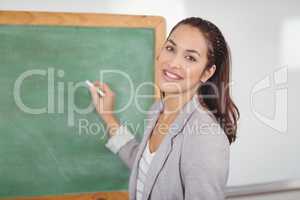 Pretty teacher writing on chalkboard in a classroom