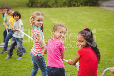 Cute pupils playing tug of war on the grass outside