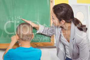 Pretty teacher helping pupil at chalkboard