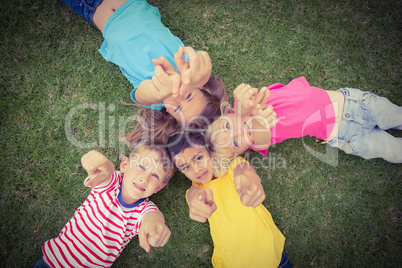 Classmates lying in grass and pointing to camera