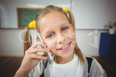 Smiling pupil phoning with smartphone in a classroom