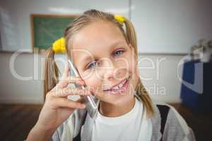 Smiling pupil phoning with smartphone in a classroom