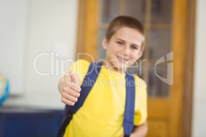 Smiling pupil with schoolbag doing thumbs up in a classroom