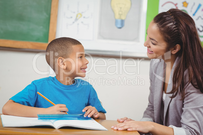 Pretty teacher helping pupil at his desk