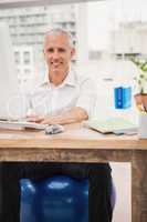 Smiling casual businessman sitting on exercise ball at desk