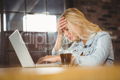 Overworked blonde sitting and using laptop