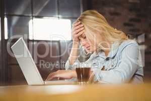 Overworked blonde sitting and using laptop