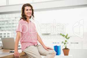 Smiling casual businesswoman leaning on desk