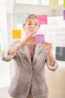 Casual businesswoman putting sticky notes on glass