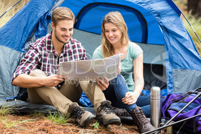 Young pretty hiker couple sitting in a tent looking at map