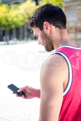 Rear view of an handsome athlete sending a text