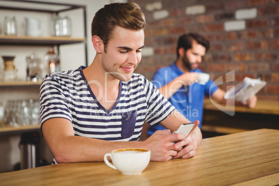 Young student enjoying a coffee and using his smartphone