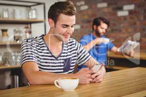 Young student enjoying a coffee and using his smartphone