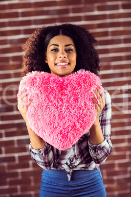 Attractive young woman holding up heart-shaped pillow