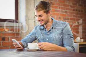 Handsome man having coffee and using smartphone