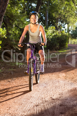 Smiling athletic brunette mountain biking on path