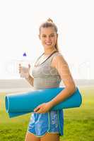 Sporty blonde holding exercise mat and water bottle