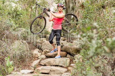 Blonde athlete carrying her mountain bike over rocks