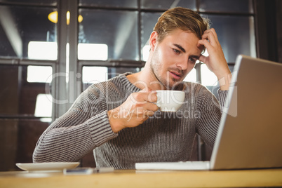 Overworked man drinking coffee and looking at laptop