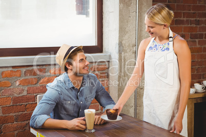 Smiling blonde waitress serving muffin to handsome hipster