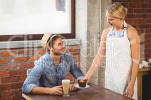 Smiling blonde waitress serving muffin to handsome hipster