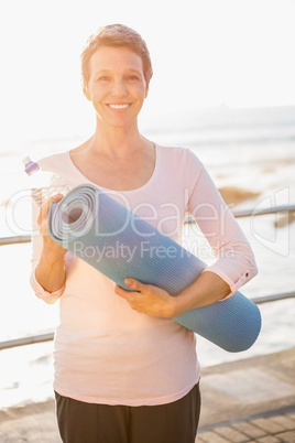 Smiling sporty woman with exercise mat