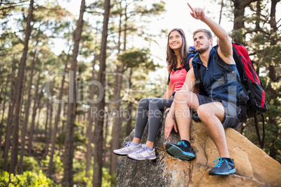 Young happy joggers sitting on rock feeling and pointing at some