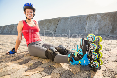 Smiling sporty blonde skater sitting on ground